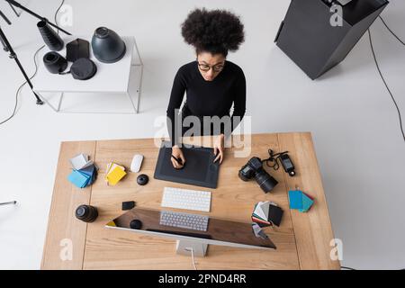 Draufsicht des kreativen afroamerikanischen Retourenhefters mit Grafiktablett im Fotostudio, Stockbild Stockfoto