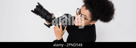 Draufsicht des fröhlichen und stilvollen afroamerikanischen Content Makers mit isolierter Digitalkamera auf grauem Banner, Stock Image Stockfoto