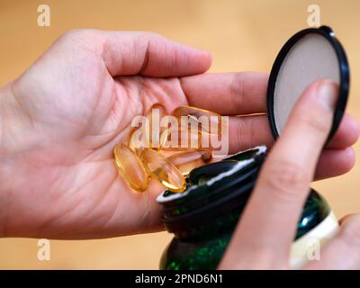 Frau, die Omega-Softgel-Kapseln aus einem Glas in die Hand schüttet. Nahaufnahme Stockfoto