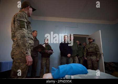 Avdiivka, Ukraine. 18. April 2023. Der ukrainische Präsident Wolodymyr Zelenskyy, Zentrum, unterhält sich mit einem verwundeten ukrainischen Soldaten, nachdem er ihm während eines Besuchs in einem Frontkrankenhaus in der Region Donezk am 18. April 2023 in Avdiivka, Ukraine, eine Militärmedaille verliehen hatte. Kredit: Pool Photo/Pressestelle Des Ukrainischen Präsidenten/Alamy Live News Stockfoto