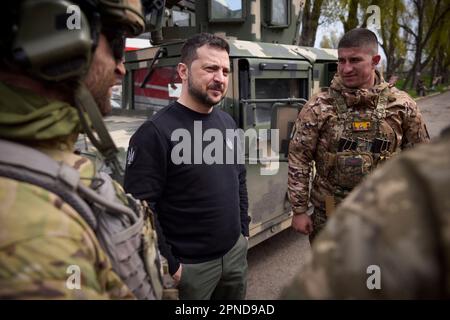 Avdiivka, Ukraine. 18. April 2023. Ukrainischer Präsident Wolodymyr Zelenskyy, Zentrum, unterhält sich mit einem ukrainischen Soldaten vor dem Evakuierungsbus Scania für verwundete Soldaten und Zivilisten während eines Besuchs an den Frontlinien in der Region Donezk am 18. April 2023 in Avdiivka, Ukraine. Kredit: Pool Photo/Pressestelle Des Ukrainischen Präsidenten/Alamy Live News Stockfoto