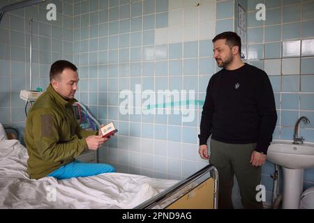 Avdiivka, Ukraine. 18. April 2023. Der ukrainische Präsident Wolodymyr Zelenskyy, richtig, unterhält sich mit einem verwundeten ukrainischen Soldaten, nachdem er ihm während eines Besuchs in einem Frontkrankenhaus in der Region Donezk am 18. April 2023 in Avdiivka, Ukraine, eine Militärmedaille verliehen hatte. Kredit: Pool Photo/Pressestelle Des Ukrainischen Präsidenten/Alamy Live News Stockfoto