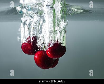 Reife Kirschen fallen ins Wasser und verursachen Spritzer und Luftblasen Stockfoto