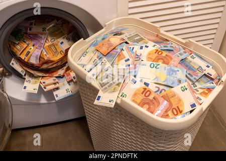 Ein großer Haufen Geld in einer offenen Waschmaschine. Der große Korb voller Geld liegt vor uns. Geldwäschekonzept. Stockfoto