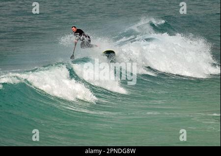Cornwall, Großbritannien. 18. April 2023. An einem warmen und windigen Nachmittag in Sennen Cove, der Heimat des Surfens, nimmt ein einsamer Surfer einen Tumble. Bildnachweis: Robert Timoney/Alamy Live News Stockfoto