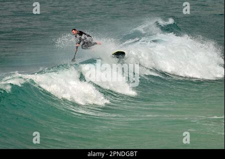 Cornwall, Großbritannien. 18. April 2023. An einem warmen und windigen Nachmittag in Sennen Cove, der Heimat des Surfens, nimmt ein einsamer Surfer einen Tumble. Bildnachweis: Robert Timoney/Alamy Live News Stockfoto