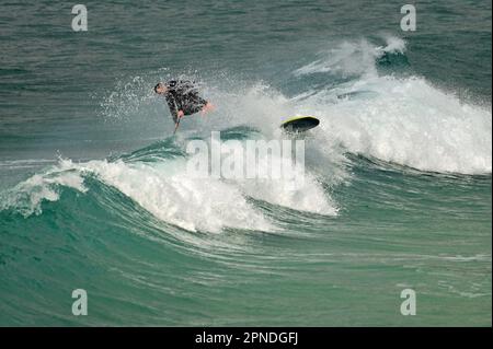 Cornwall, Großbritannien. 18. April 2023. An einem warmen und windigen Nachmittag in Sennen Cove, der Heimat des Surfens, nimmt ein einsamer Surfer einen Tumble. Bildnachweis: Robert Timoney/Alamy Live News Stockfoto