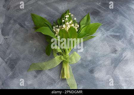 Blütenzusammensetzung. Ein Strauß Lilien aus dem Tal. Weiße Frühlingsblumen auf grauem Holzhintergrund. Farbenfrohes festliches Design. Das Konzept von Mutter' Stockfoto