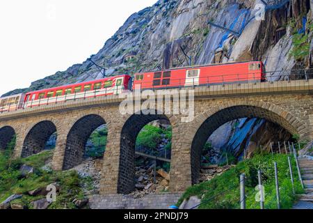 Roter Zug, der an der Teufelsbrücke in St. vorbeifährt Gotthard Pass auf den Schweizer Alpen in Andermatt, Schweiz Stockfoto