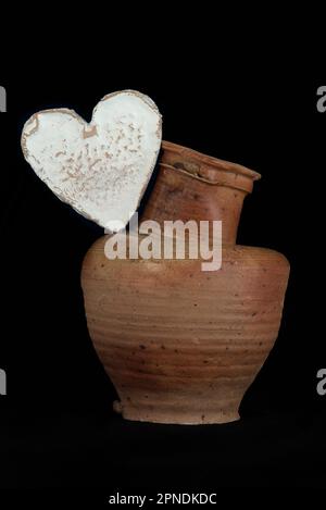 Stillleben mit einem Neufchatel Normand-Käse (A.O.P.) und einem Steingut-Krug auf schwarzem Hintergrund Stockfoto