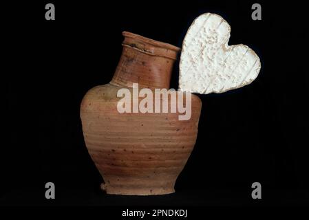 Stillleben mit einem Neufchatel Normand-Käse (A.O.P.) und einem Steingut-Krug auf schwarzem Hintergrund Stockfoto