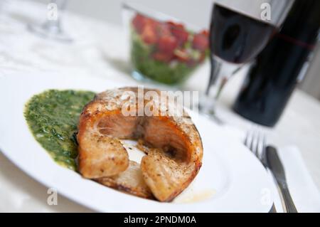 Lachsfilet mit Petersiliensoße serviert mit Rotwein Stockfoto