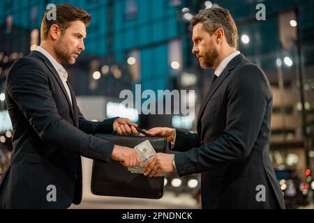 Ein Geschäftsmann, der seinem Partner Geld gibt, während er einen Vertrag schließt. Ein Geschäftsmann, der draußen Geld spendet. Sie zählen uns Dollarscheine, Geld, Finanzmitarbeiter Stockfoto