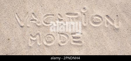 Sand-Hintergrund. Urlaubsmodus auf Sand geschrieben. Stockfoto