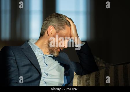 Gestresster Geschäftsmann mit Kopfschmerzen im Home Office. Ein müder Geschäftsmann macht Überstunden und hat Kopfschmerzen. Das Porträt des Senioren leidet an Kopfschmerzen Stockfoto