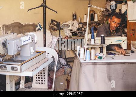 Marrakesch, Marokko - 02. Januar 2020: Unbekannter Mann, der mit Nähmaschinen arbeitet und Kleidung für den Verkauf in seiner Werkstatt und am Marktstand repariert Stockfoto