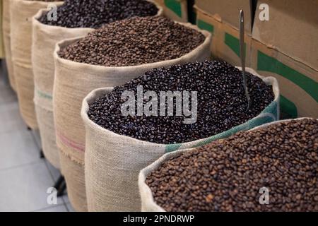 Frisch geröstete Kaffeebohnen mit einem Metalllöffel, in Jutesäcken. Nahaufnahme mit offenem Kaffeebeutel. Arabische Kaffeebohnen in der Tüte Stockfoto