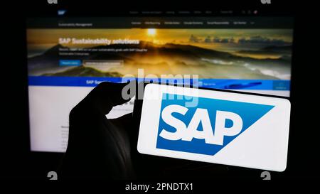 Person, die ein Mobiltelefon mit dem Logo des deutschen Softwareunternehmens SAP SE auf dem Bildschirm vor der geschäftlichen Webseite hält. Konzentrieren Sie sich auf das Display des Telefons. Stockfoto