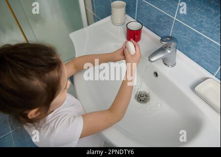 Handhygiene und Virusinfektionsprophylaxe. Blick von oben auf ein kleines Mädchen, das sich die Hände wäscht, mit Seifenbügel im Badezimmer Stockfoto