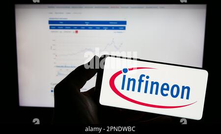 Person, die ein Mobiltelefon mit dem Logo des Halbleiterunternehmens Infineon Technologies AG auf dem Bildschirm vor der Webseite hält. Konzentrieren Sie sich auf das Display des Telefons. Stockfoto