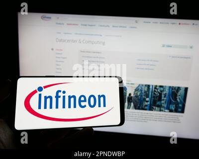 Person, die ein Smartphone mit dem Logo des Halbleiterunternehmens Infineon Technologies AG auf dem Bildschirm vor der Website hält. Konzentrieren Sie sich auf das Display des Telefons. Stockfoto