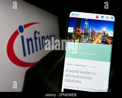Person, die ein Smartphone mit einer Webseite des Halbleiterunternehmens Infineon Technologies AG auf dem Bildschirm mit Logo hält. Konzentrieren Sie sich auf die Mitte des Telefondisplays. Stockfoto