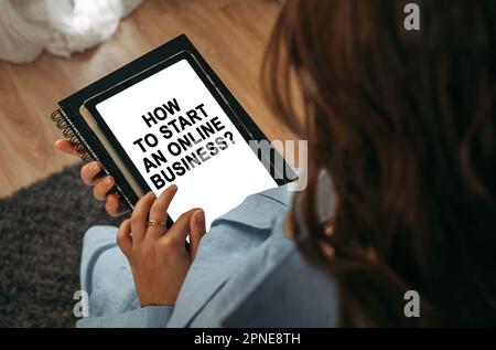 Online-Lernkonzept. Eine Frau hält ein Tablet in der Hand auf dem Bildschirm, auf dem es geschrieben ist – How to Start an Online Business Stockfoto