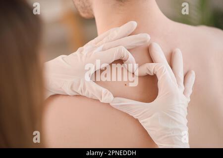 Dermatologe untersucht Muttermal auf dem Rücken eines jungen Mannes in der Klinik, Nahaufnahme Stockfoto