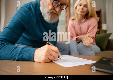 Seniorenpaar Füllt Formular Aus Und Unterschreibt Papiere, Die Drinnen Sitzen Stockfoto