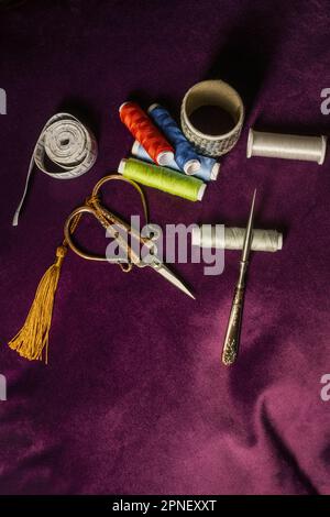 Nähutensilien, Scheren, Fadenspulen, Maßband, Nadeln, Auf dunkellilafarbenem Samtstoff angeordnet Stockfoto
