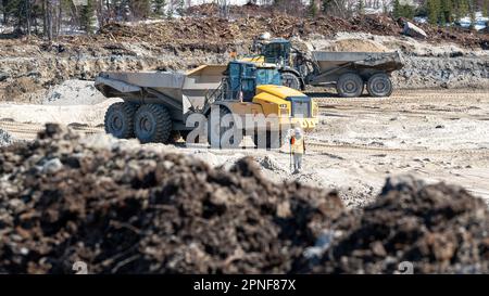 Dumper fahren auf einer Baustelle und ein Landvermesser an einem sonnigen Tag Stockfoto