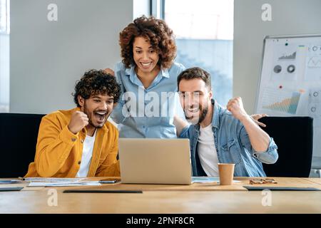 Aufgeregte Mitarbeiter eines Unternehmens, die mehrere Rassen vertreten, sich im kreativen Büro emotional zeigen, sich über den Erfolg freuen, gute Verkaufsergebnisse feiern, finanzielle Ziele erreichen, gutes Geschäft, Vertrag Stockfoto