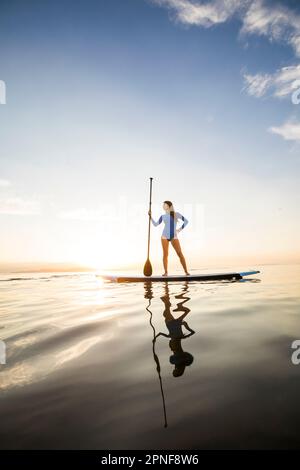 Eine Frau, die bei Sonnenuntergang auf dem Paddleboard steht Stockfoto