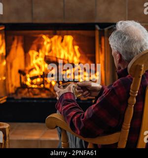 Seniorenmann, der sich vor dem Holzkamin entspannt Stockfoto
