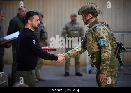 Kherson, Ukraine. 19. April 2023. Zeigt, wie der ukrainische Präsident Wolodymyr Zelensky (L) während seines Besuchs in der schwer beschießten Frontstadt Avdiivka in der Region Donezk inmitten der russischen Invasion der Ukraine am Dienstag, den 18. April 2023, Soldaten verlieh. Foto: Pressestelle des ukrainischen Präsidenten/UPI. Kredit: UPI/Alamy Live News Stockfoto