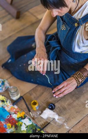 Künstlerin malt auf einer Leinwand ein blaues abstraktes Gemälde. Kreative Frau, die in ihrem Kunstatelier auf dem Boden arbeitet. Stockfoto