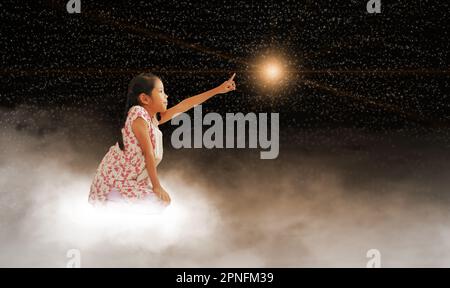 Ein Mädchen greift nach dem Stern, sitzt auf einer Wolke am dunklen Himmel, nachts. Konzepte, wie man seinen Traum, seinen Wunsch, sein Ziel und das Unmögliche erfüllt. Stockfoto