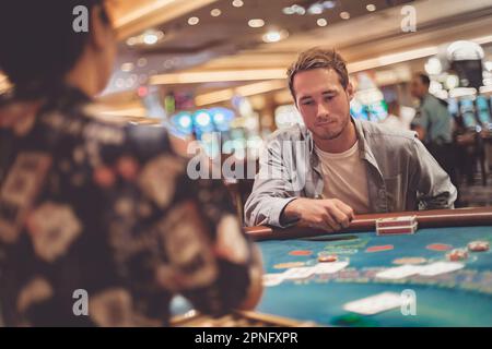 Ein junger Mann im Casino spielt Blackjack mit Karten und Chips. Indoor-Porträt eines Spielers mit Dealer Stockfoto