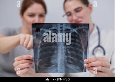 Der Arzt konsultiert eine kaukasische Frau und kommentiert die Röntgenaufnahme der Lunge. Stockfoto