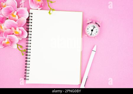 Leeres offenes Notizbuch und Uhr mit rosafarbener Orchidee für Ihren Text oder Ihre Nachricht. Stockfoto