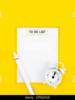 Aufgabenliste mit Wecker und Stift auf gelbem Hintergrund. Stockfoto
