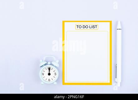 Leere Papiernotiz für Aufgabenliste oder Wunschliste und Wecker mit Stift auf grauem Hintergrund. Stockfoto