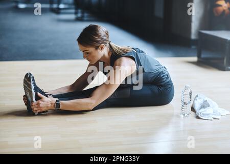 Geben Sie harte Arbeit ein, sehen Sie sich die Ergebnisse an. Eine attraktive junge Frau, die sich während ihres Trainings im Fitnessstudio dehnt. Stockfoto