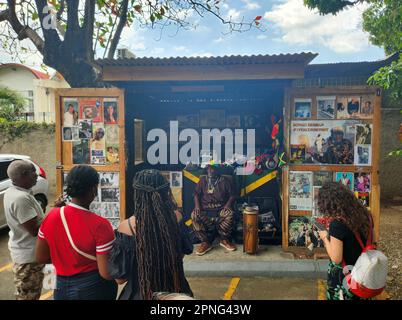 Kingston, Jamaika. 25. März 2023. Auf dem Gelände des Bob Marley Museum sitzt der 79-jährige Reggae-Perkussionist Herman Davis, bekannt als Bongo Herman, in seinem Stand vor einer Gruppe von Touristen. Er verkauft dort Musikaufnahmen und Souvenirs und spricht über seine lange Musikkarriere. (Zu dpa-Korr 'Catch a Fire': Als Reggae vor 50 Jahren in die Welt ging') Kredit: Nick Kaiser/dpa/Alamy Live News Stockfoto