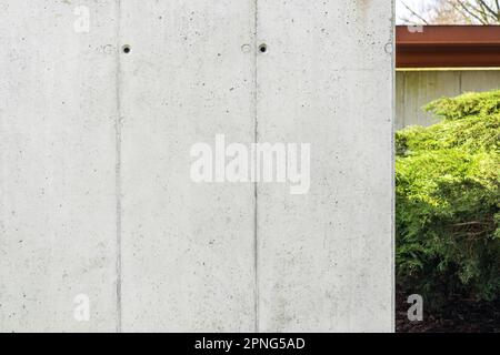 Architektonischer Schalbeton. Beton, graue Wand mit sichtbaren Schalungslöchern. Grüne Büsche im Hintergrund Stockfoto