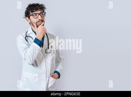 Arzt denkt mit der Hand am Kinn. Junger Arzt denkt und schaut nach isoliert, pensiver Arzt, der isoliert nach oben schaut Stockfoto
