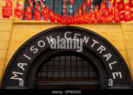 Vietnam: Flaggen fliegen über dem Eingang zum Hoa Lo Gefängnismuseum (das alte französische Maison Centrale), Hanoi. Die französische Kolonialverwaltung baute 1896 das Hoa Lo Gefängnis. Ursprünglich sollten 450 Gefangene festgehalten werden, und in den 1930er Jahren war die Zahl der Inhaftierten auf fast 2.000 angestiegen, die politische Gefangene mit großer Mehrheit. Das Hoa Lo Gefängnis wurde während des Zweiten Indochina-Krieges als Ort der Inhaftierung für niedergeschlagene US-Piloten bekannt, die das Gefängnis ironischerweise „Hanoi Hilton“ nannten. Stockfoto