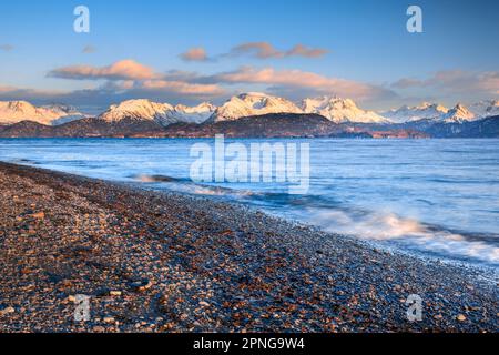 Abendliche Atmosphäre im Homer Spit mit Blick über den Steinstrand und die Kachemak Bay zu den Kenai Mountains im warmen Abendlicht im Hintergrund Stockfoto