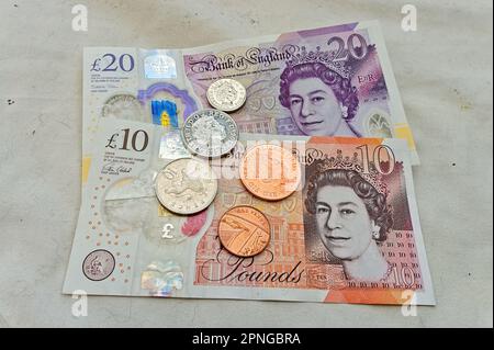 Britische 10-Pfund- und 20-Pfund-Banknoten und -Münzen mit der verstorbenen Königin auf hellem Hintergrund Stockfoto