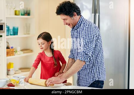 Ich kann es kaum erwarten, zu sehen, wann die Pizza fertig ist. Ein Vater mittleren Alters und seine Tochter bereiten eine Pizza zu, die in den Ofen in der Küche zu Hause geht. Stockfoto